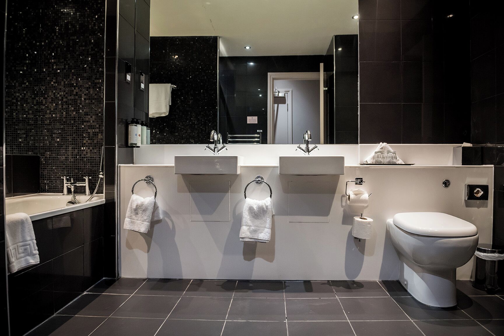 Un baño moderno con un espejo grande, tres lavamanos, un inodoro y una zona de ducha.