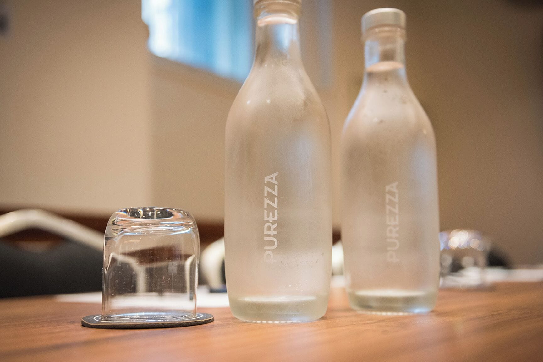 Tres botellas de vidrio con la etiqueta "PUREZZA" sobre una superficie de madera.