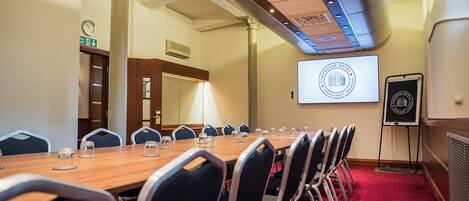 Una sala de conferencias con una mesa larga, sillas, una pantalla de proyector y una pizarra.