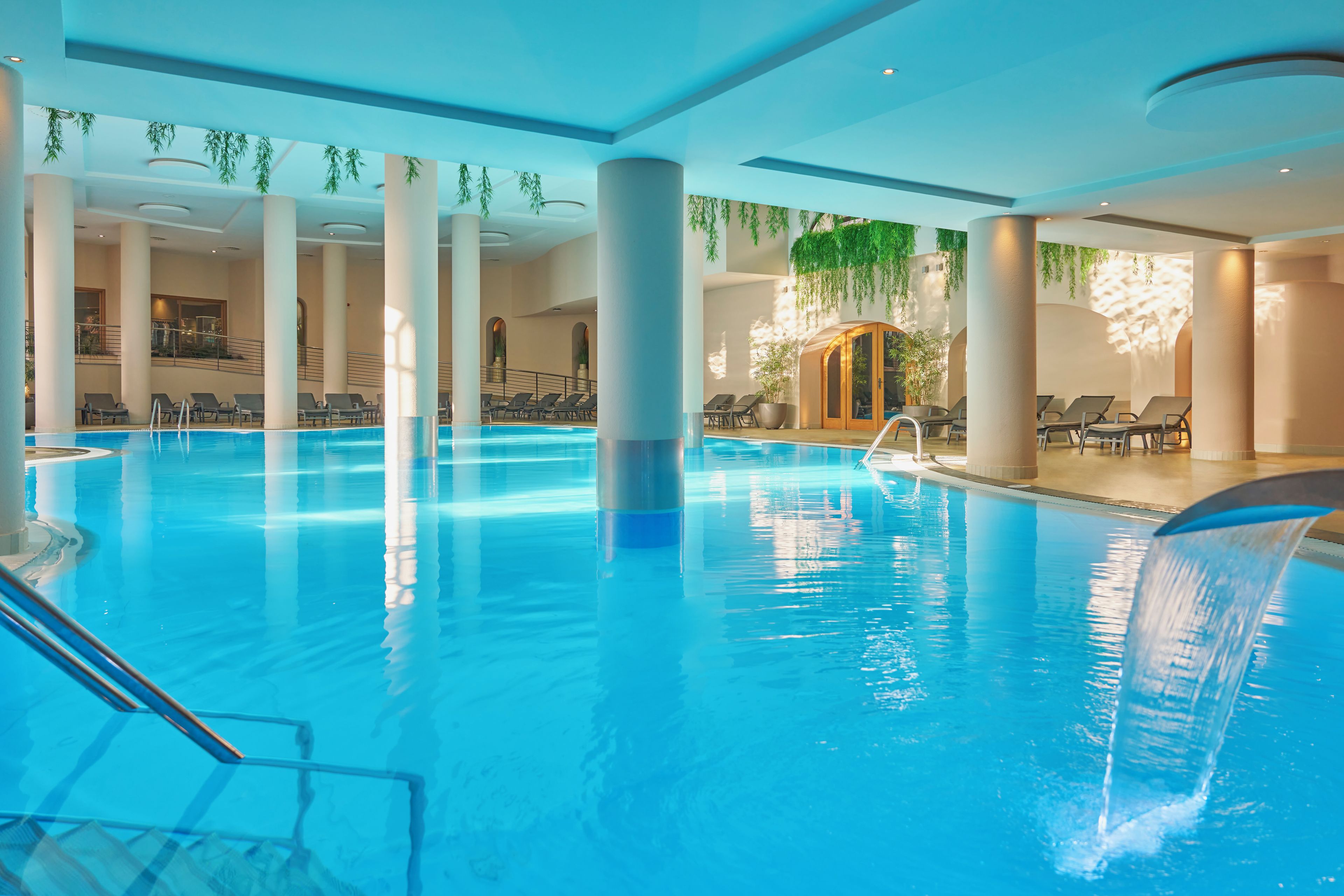 Una piscina interior con agua cristalina, rodeada de sillones de descanso y una zona de estar cubierta.