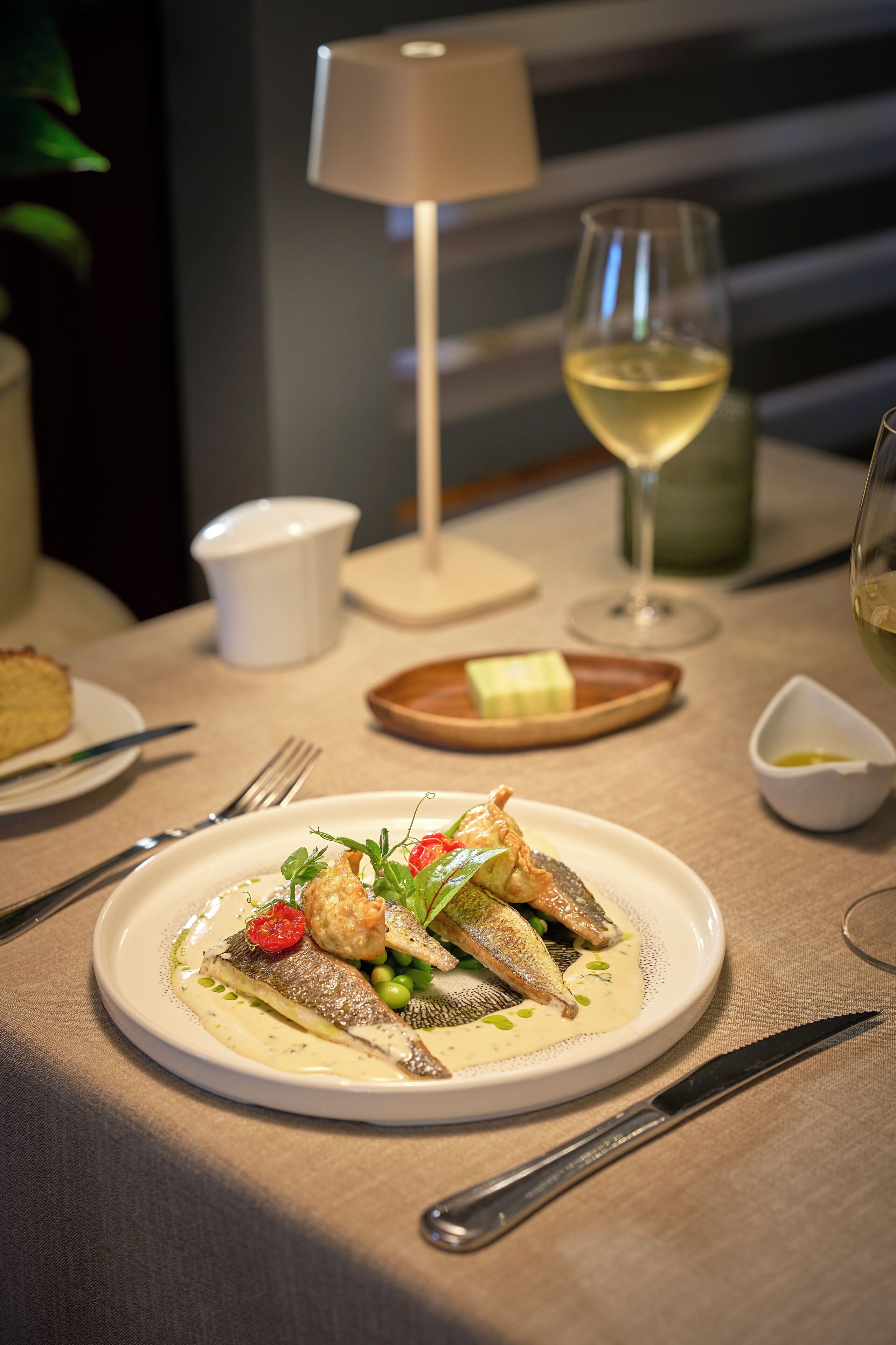 A dining table with a plate of food, a wine glass, and a lamp.