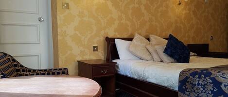 A hotel room with a bed, bedside table, lamp, and a round wooden table.