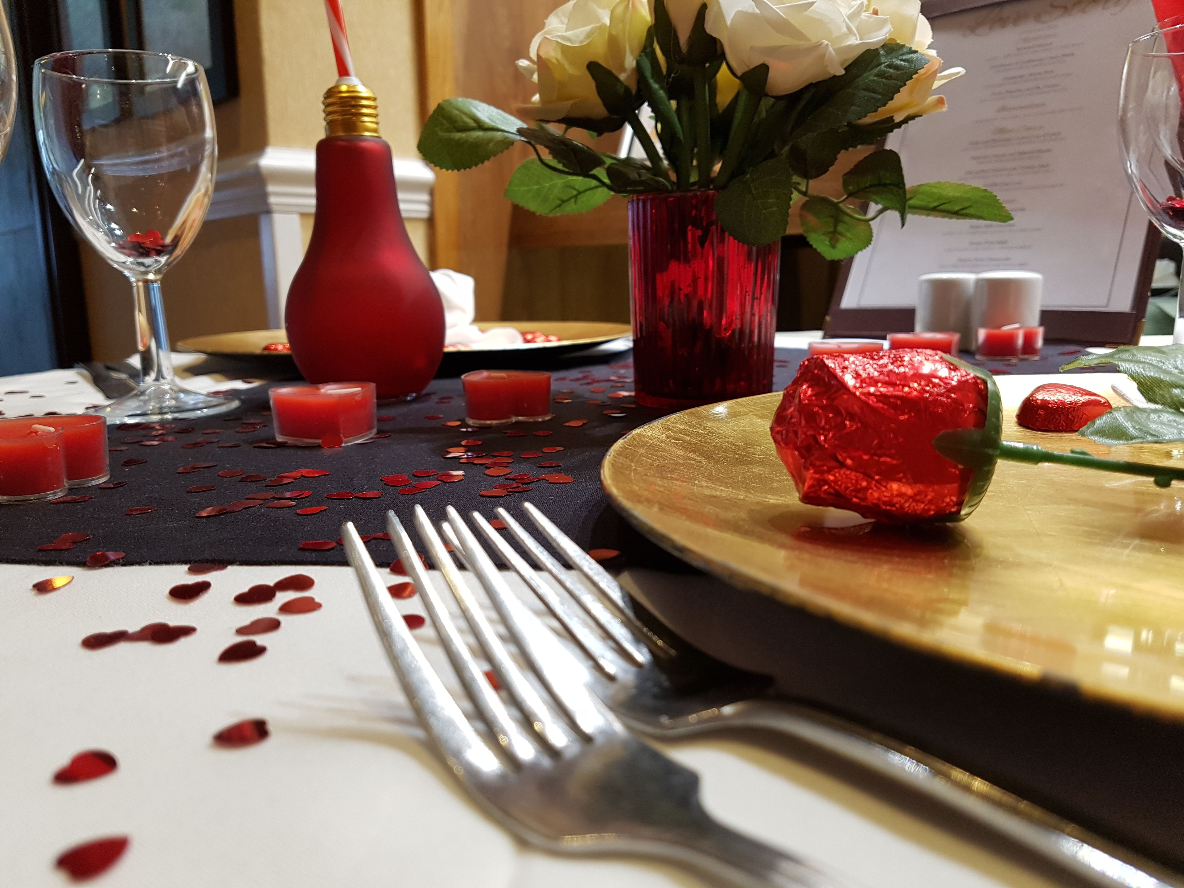 Una tavola apparecchiata per la cena, con una rosa rossa, un bicchiere di bevanda rossa e un menu.