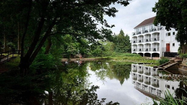 Una vista tranquila junto al río, con un edificio blanco de varios balcones y una puerta roja.