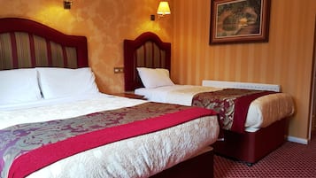 A hotel room with two beds, each with a headboard, white bedding, and a red throw blanket. There are wall-mounted lamps and a framed picture on the wall.