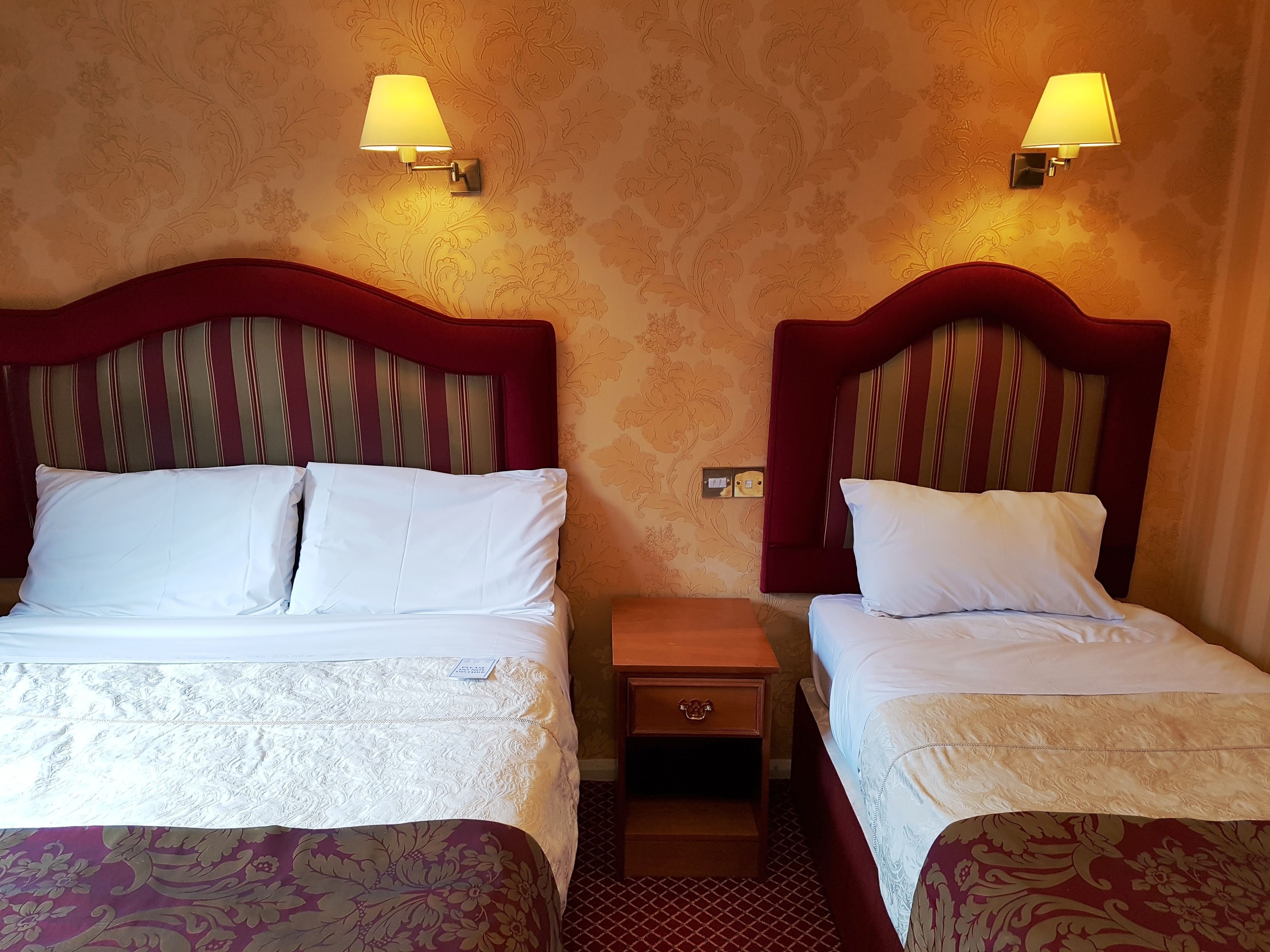 Une chambre d’hôtel avec deux lits, chacun doté d’une tête de lit rouge et de draps blancs. Deux lampes murales sont fixées de part et d’autre des lits.