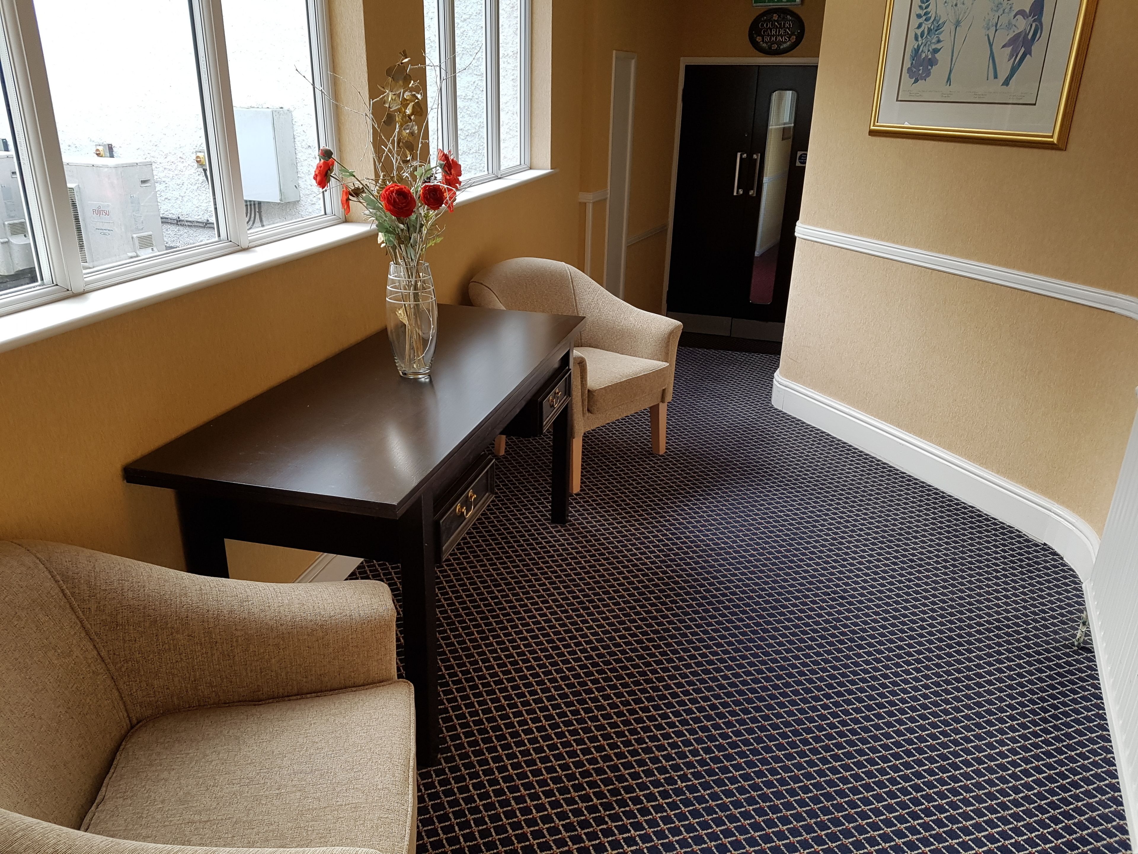 A room with a dark wooden table, beige armchairs, a vase with red flowers, and a patterned carpet.