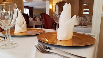 Una mesa de comedor dispuesta con platos dorados, servilletas blancas y cubiertos en un espacio bien iluminado, con papel tapiz estampado y un espejo.