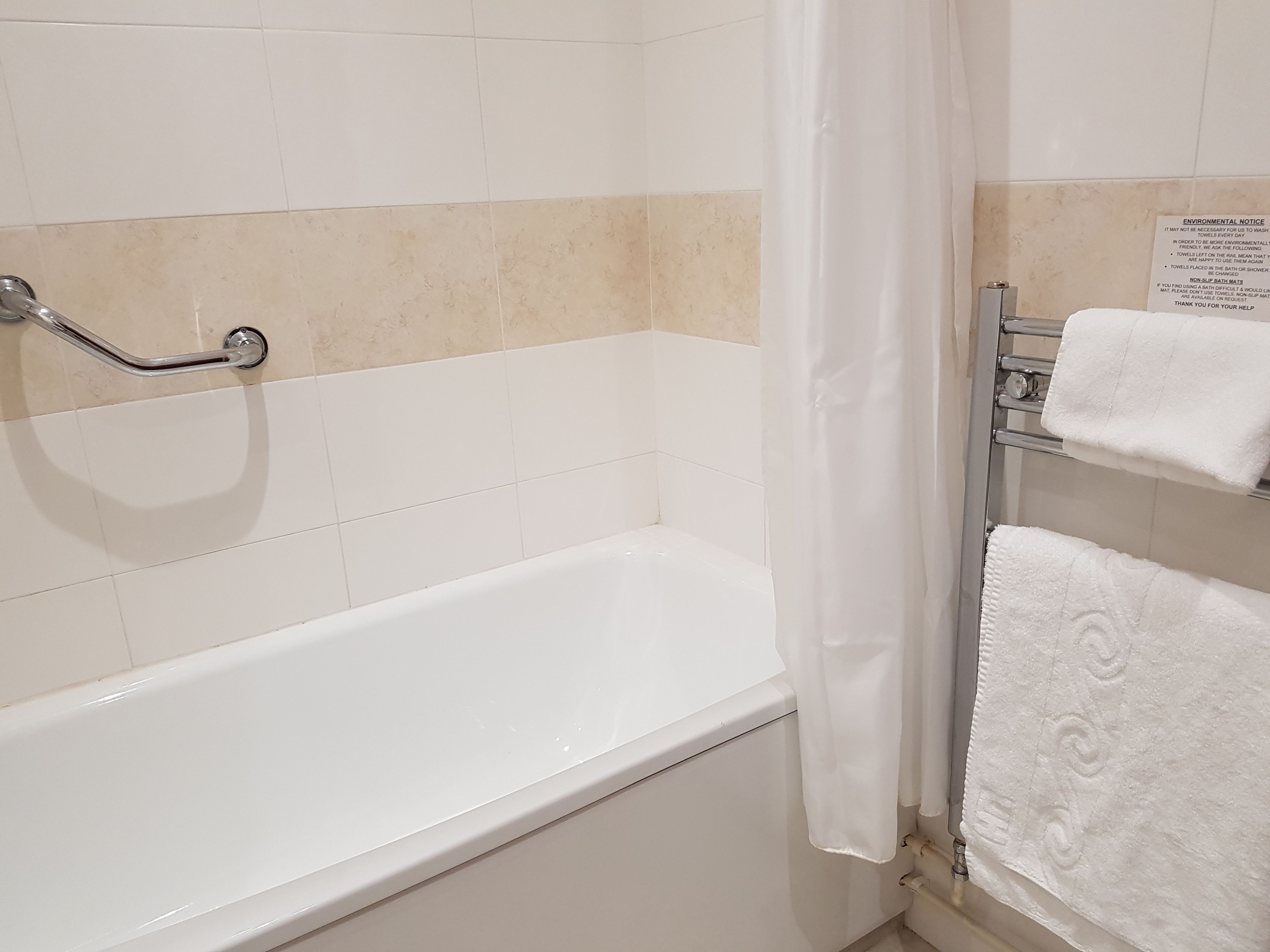 Une salle de bain avec une baignoire blanche, une barre d’appui, un porte-serviettes avec deux serviettes et un panneau sur le mur.