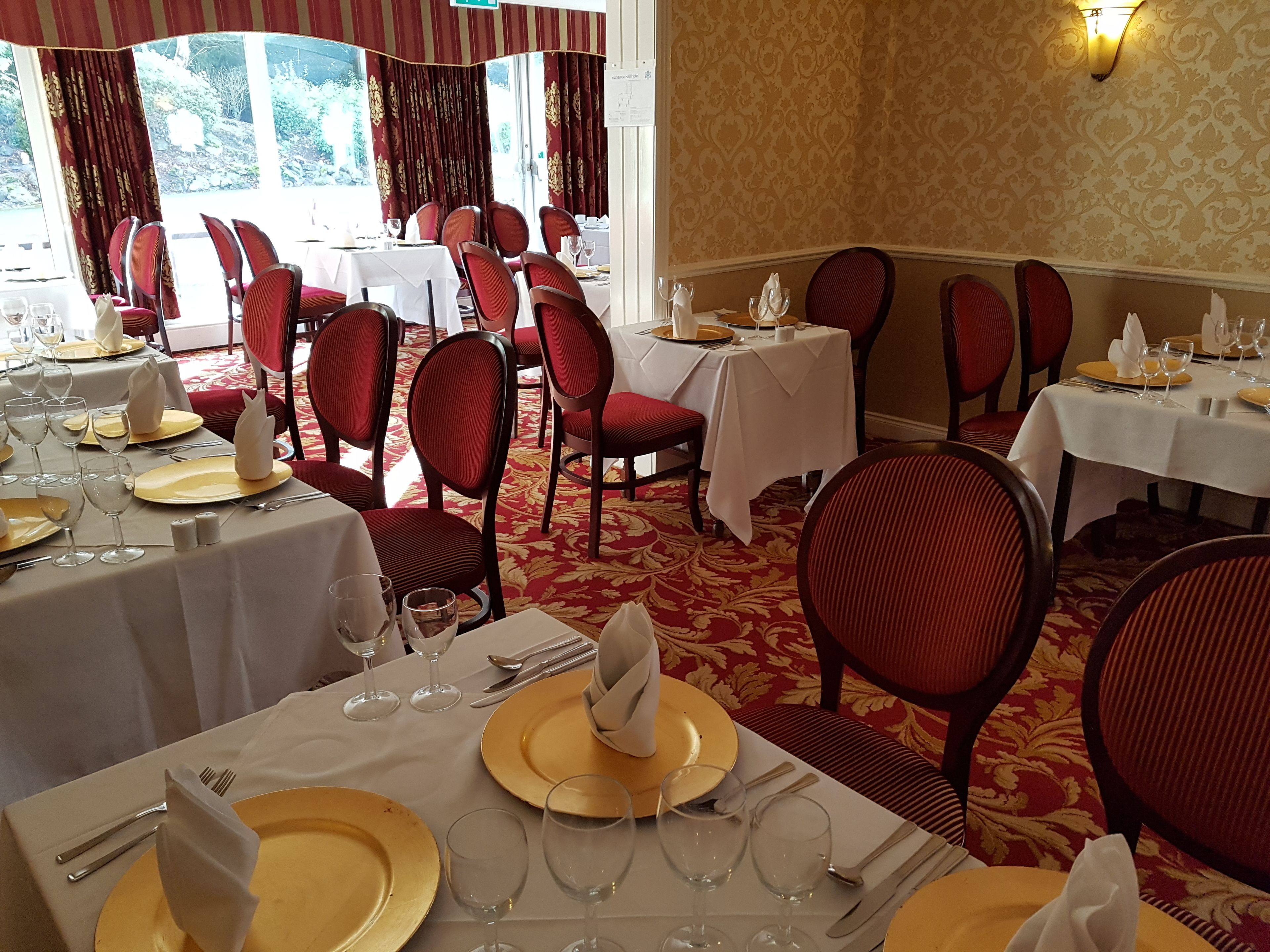 A restaurant with multiple tables set for dining, featuring red chairs and gold table settings.