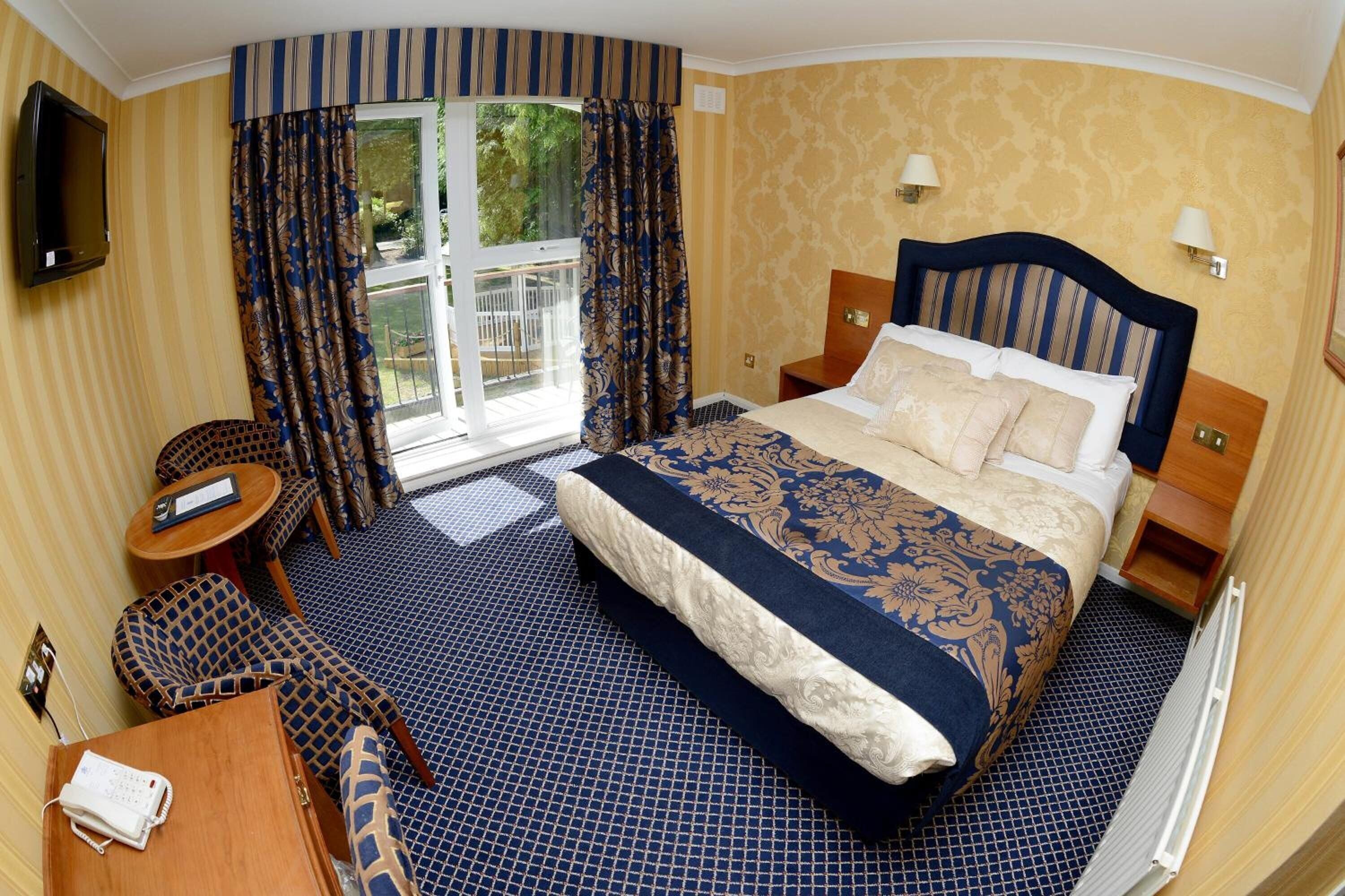 Ein Hotelzimmer mit einem großen Bett, einem an der Wand montierten Fernseher, einem kleinen Tisch, einer Couch und einem Fenster mit Vorhängen.