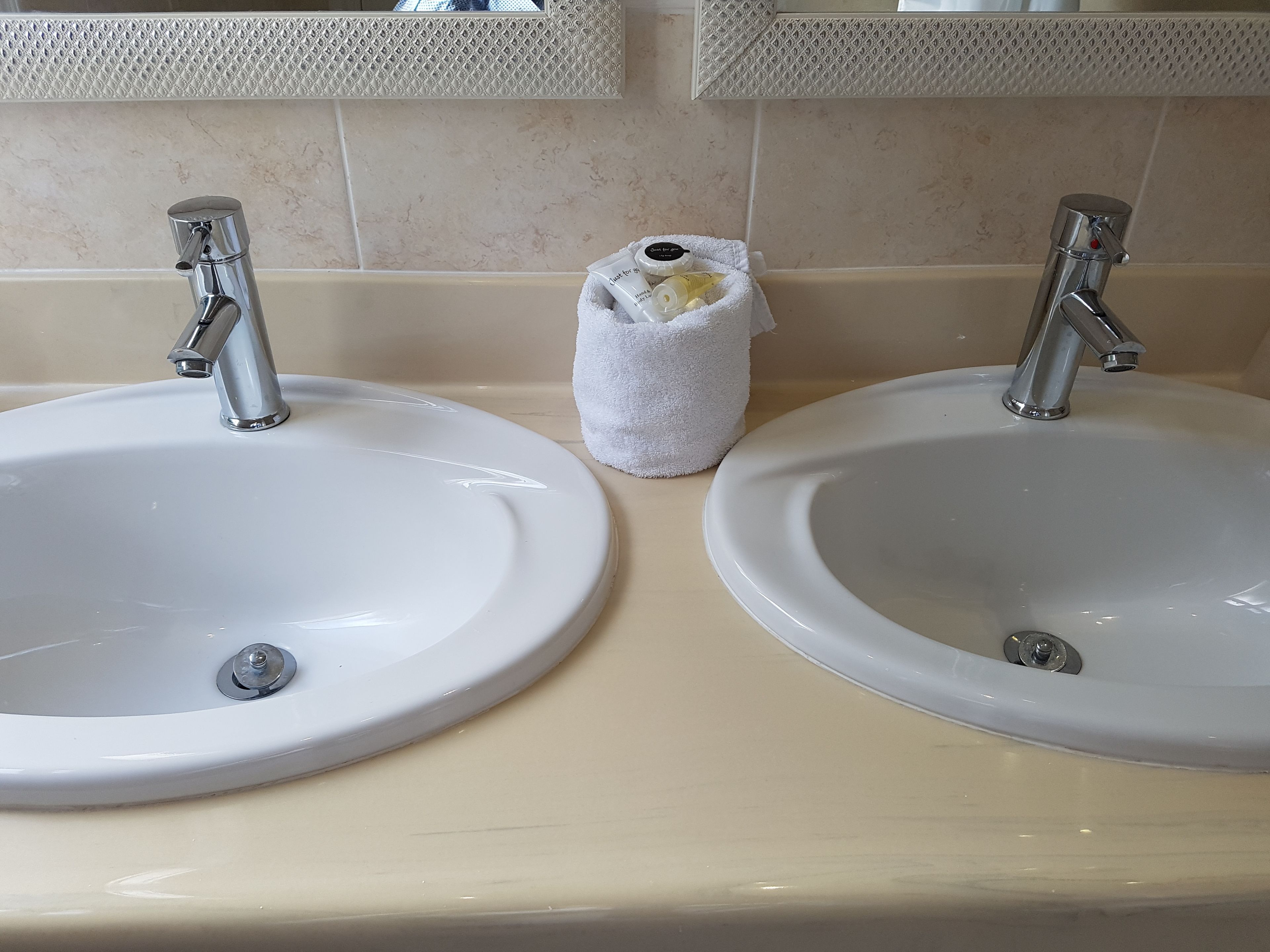 Two white sinks with chrome faucets, a beige countertop, and a small white towel bag with toiletries.