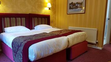 A hotel room with a large bed, a red headboard, a wall-mounted lamp, and a framed picture on the wall.