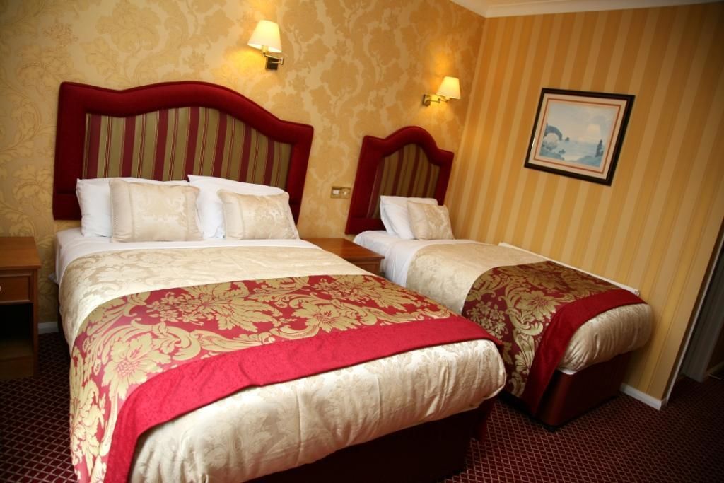Une chambre d’hôtel avec deux lits, chacun recouvert d’une courtepointe rouge et or, et un tableau accroché au mur.