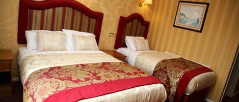 Une chambre d’hôtel avec deux lits, chacun recouvert d’une courtepointe rouge et or, et un tableau accroché au mur.