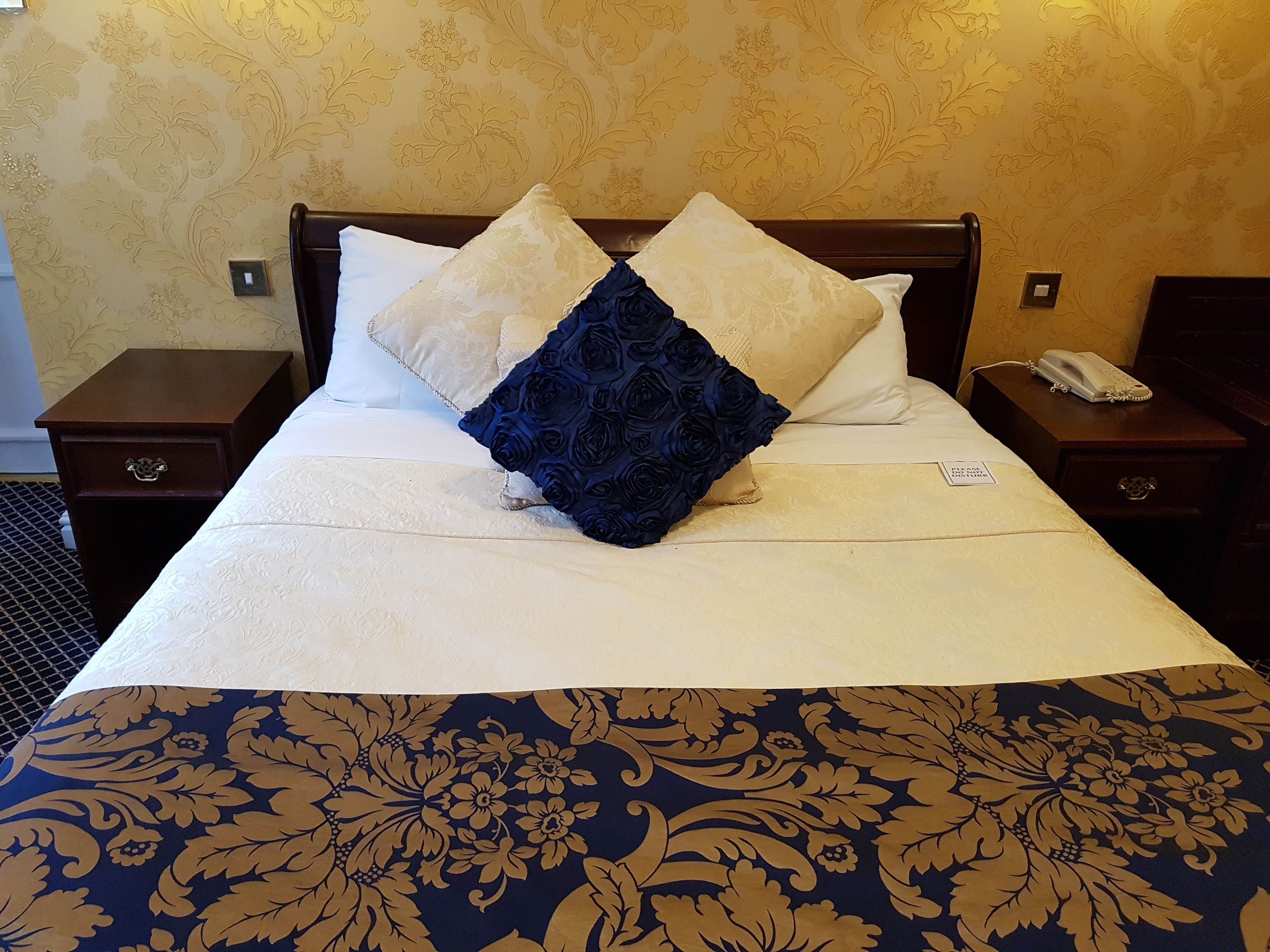 Camera d'albergo con un letto grande, due comodini, un telefono e una parete con motivo floreale.