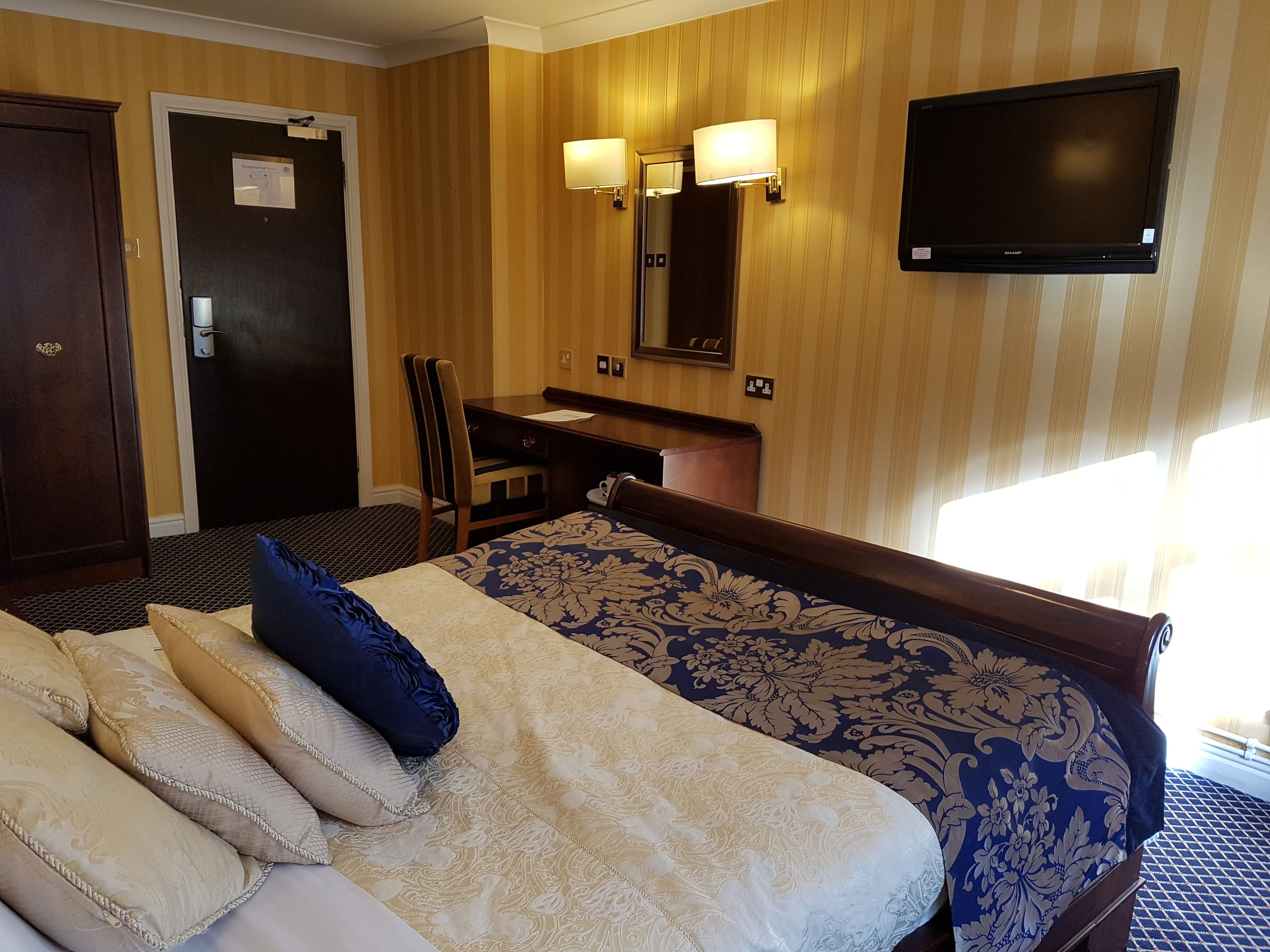 Una habitación de hotel con una cama, un escritorio, una silla, un televisor y una puerta.