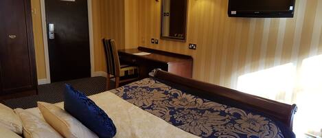 Una habitación de hotel con una cama, un escritorio, una silla, un televisor y una puerta.