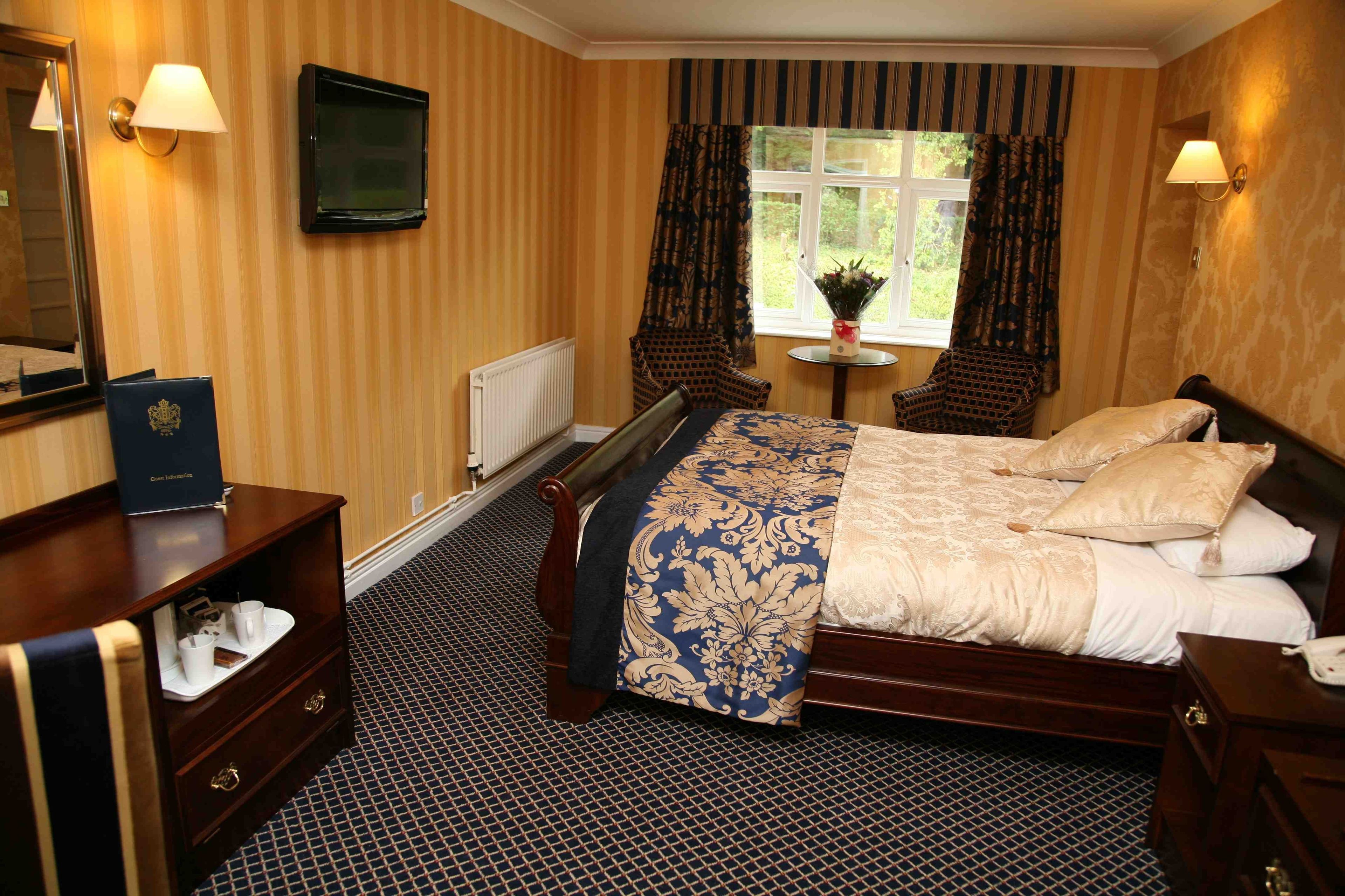 Habitación de hotel con una cama grande, una mesita de noche, un aparador, un espejo, un televisor y una ventana con cortinas.