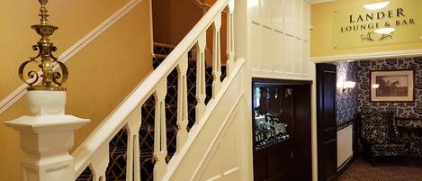 A staircase with white balusters leading to a landing with a sign for 'Lander Lounge & Bar'.