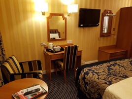 A hotel room with a bed, a desk with a chair, a television mounted on the wall, and a mirror above the desk.
