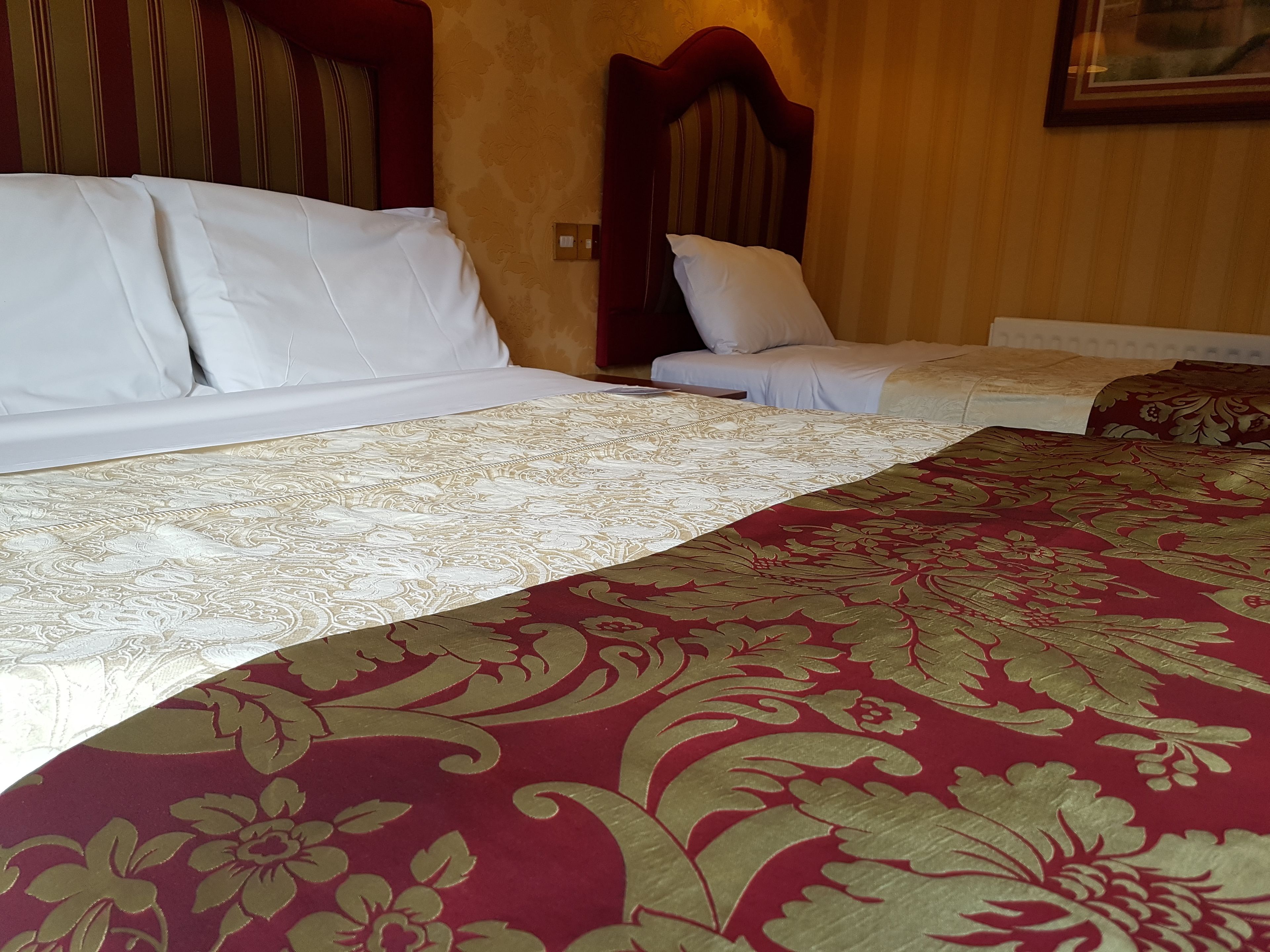 A hotel room with a large bed, two smaller beds, wooden headboards, and a patterned bedspread.