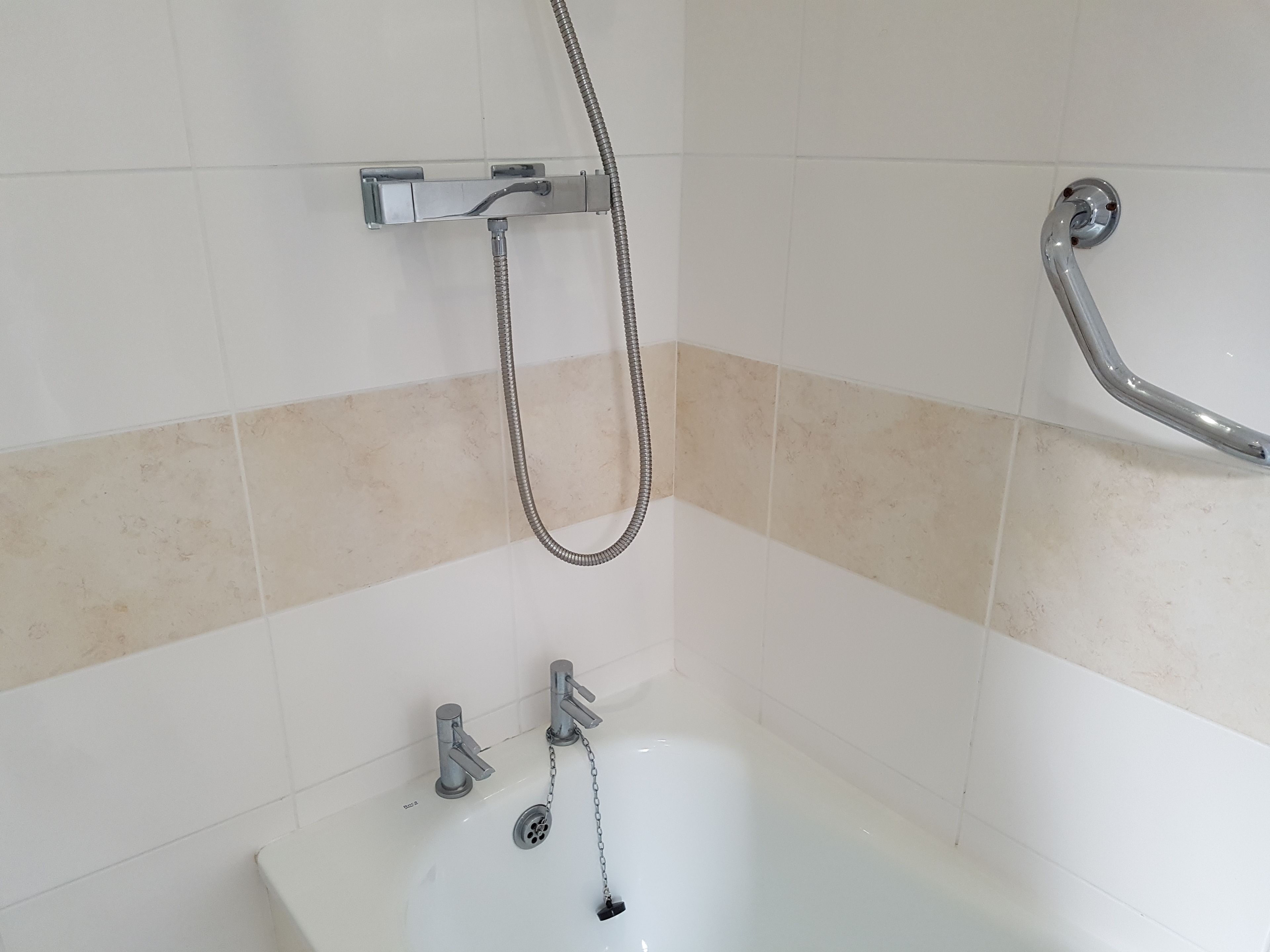 Une salle de bain équipée d’une baignoire, de deux robinets, d’une pomme de douche et d’une barre d’appui.