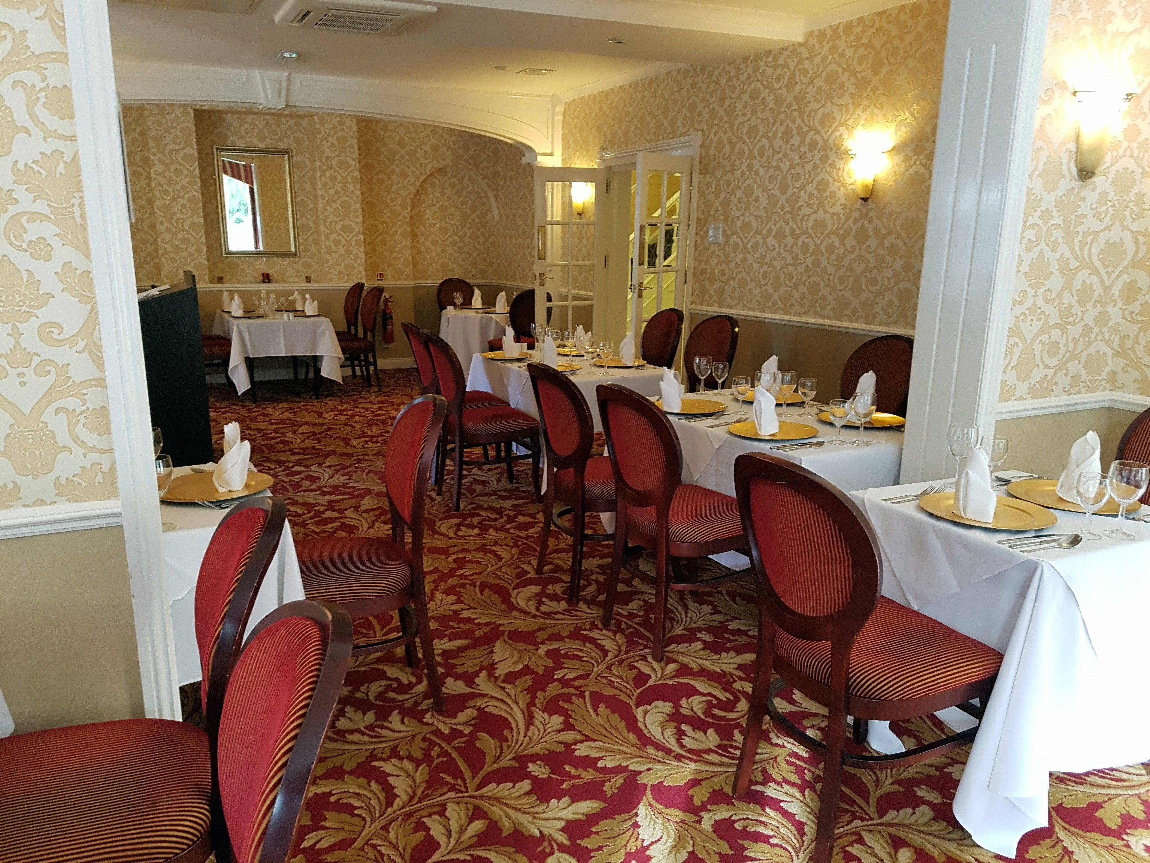 Een formele eetzaal met vier gedekte tafels, rode gestoffeerde stoelen en een vloerbedekking.