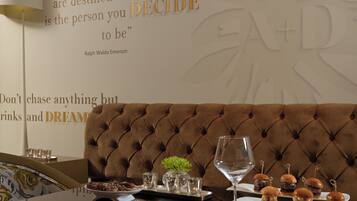 A dining area with a brown tufted sofa, a glass wine glass, and a tray of mini burgers.