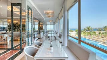 Habitación de hotel moderna con un ventanal grande que da a una piscina y vistas al mar.