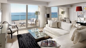 A spacious living room with a large sofa, a coffee table, and a view of the sea through floor-to-ceiling windows. - Divani Apollon Palace & Thalasso (Vari-Voula-Vouliagmeni)