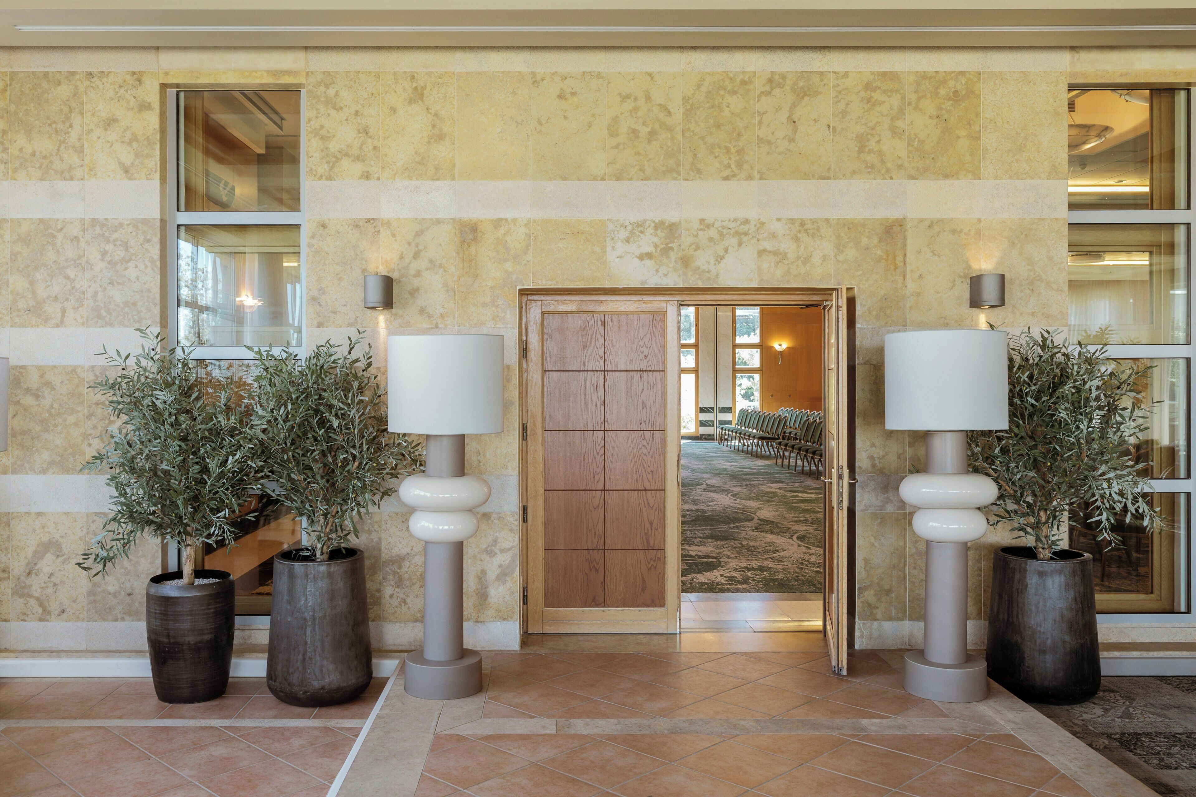 Un hall con puerta de madera, plantas en macetas y lámparas fijadas a la pared.