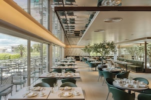 A modern restaurant with multiple dining areas, large windows, and indoor plants.