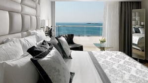 A modern hotel room with a large bed, a view of the sea, and a balcony with a glass table. - Divani Apollon Palace & Thalasso (Vari-Voula-Vouliagmeni)