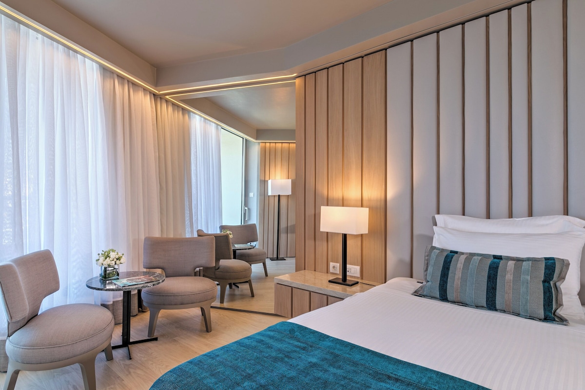 A hotel room with a bed, two armchairs, a small table, and a lamp.