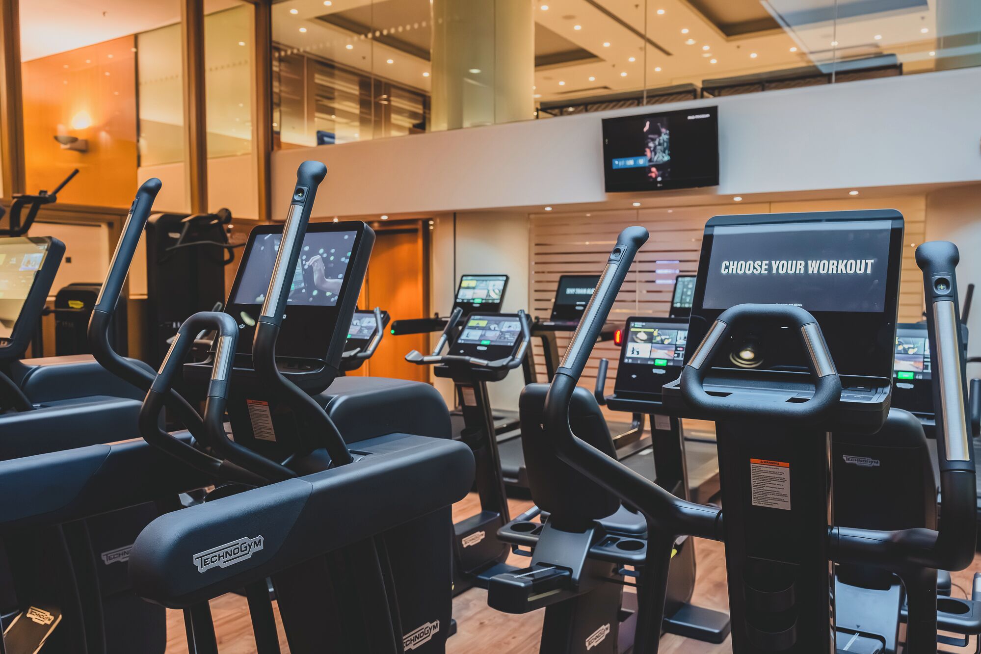 A gym with multiple treadmills and exercise bikes, each equipped with digital screens and control panels.