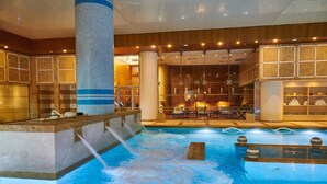 An indoor pool with a waterfall feature, surrounded by stone walls and seating areas. - Divani Apollon Palace & Thalasso (Vari-Voula-Vouliagmeni)
