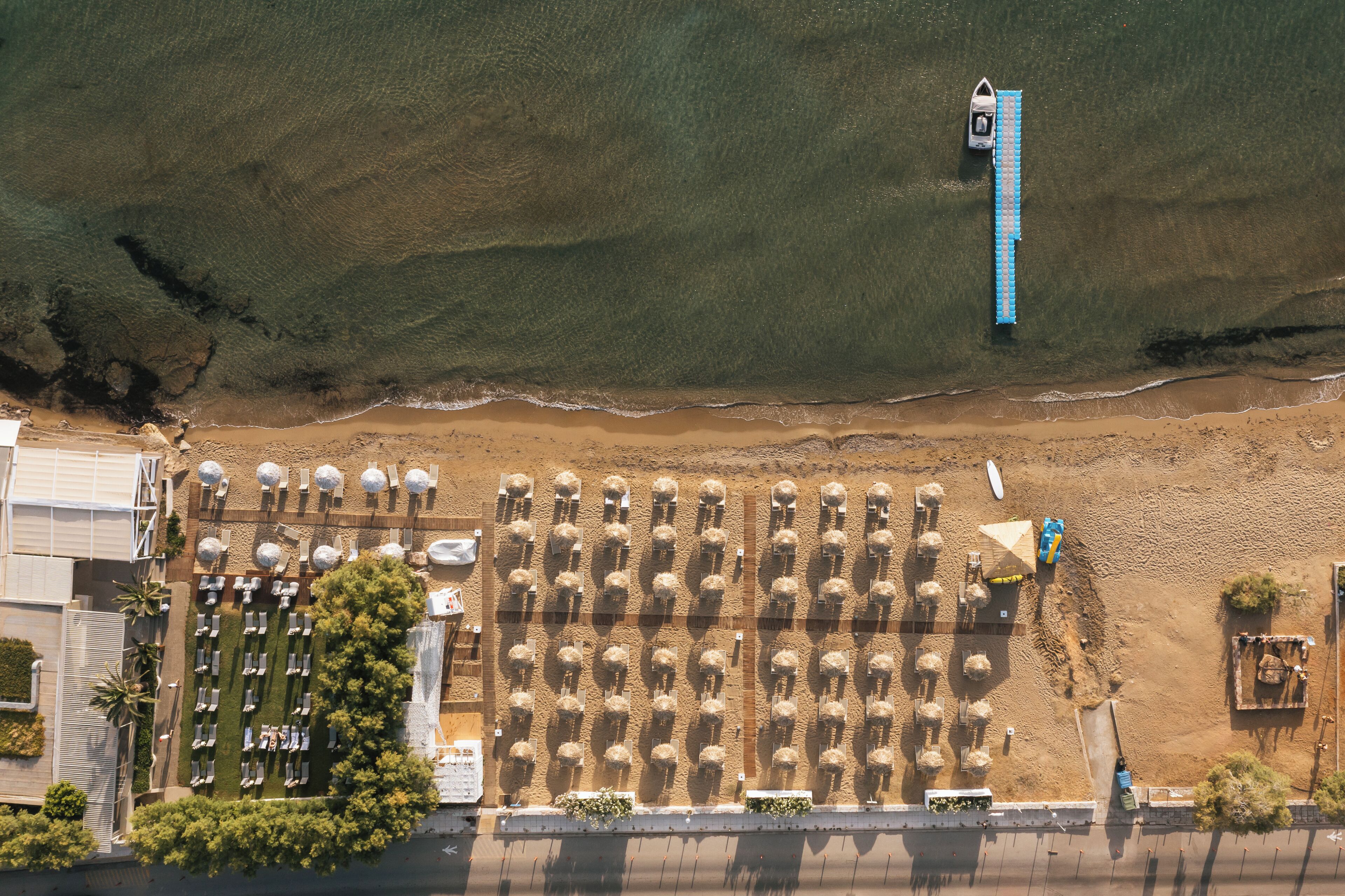 An aerial view of a beach with rows of umbrellas and lounge chairs, a lifeguard tower, and a sandy beach area.