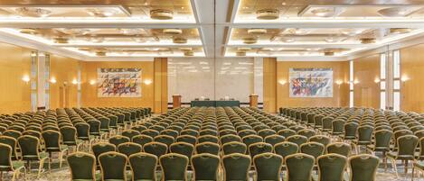 A conference room with rows of green chairs, a stage with a table, and a large poster on the wall.