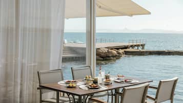 Mesa lista para comer con vista al mar y un muelle al fondo.