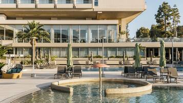 Un hotel moderno con zona de piscina, mobiliario exterior y un edificio grande de varios pisos.