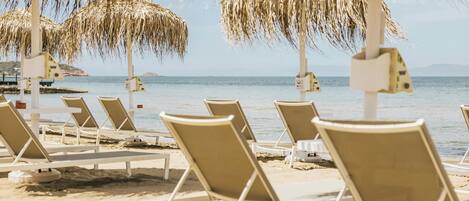 Una playa con filas de sillas de playa blancas y sombrillas de paja.