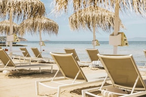 A beach with rows of white lounge chairs and straw umbrellas. - Divani Apollon Palace & Thalasso (Vari-Voula-Vouliagmeni)