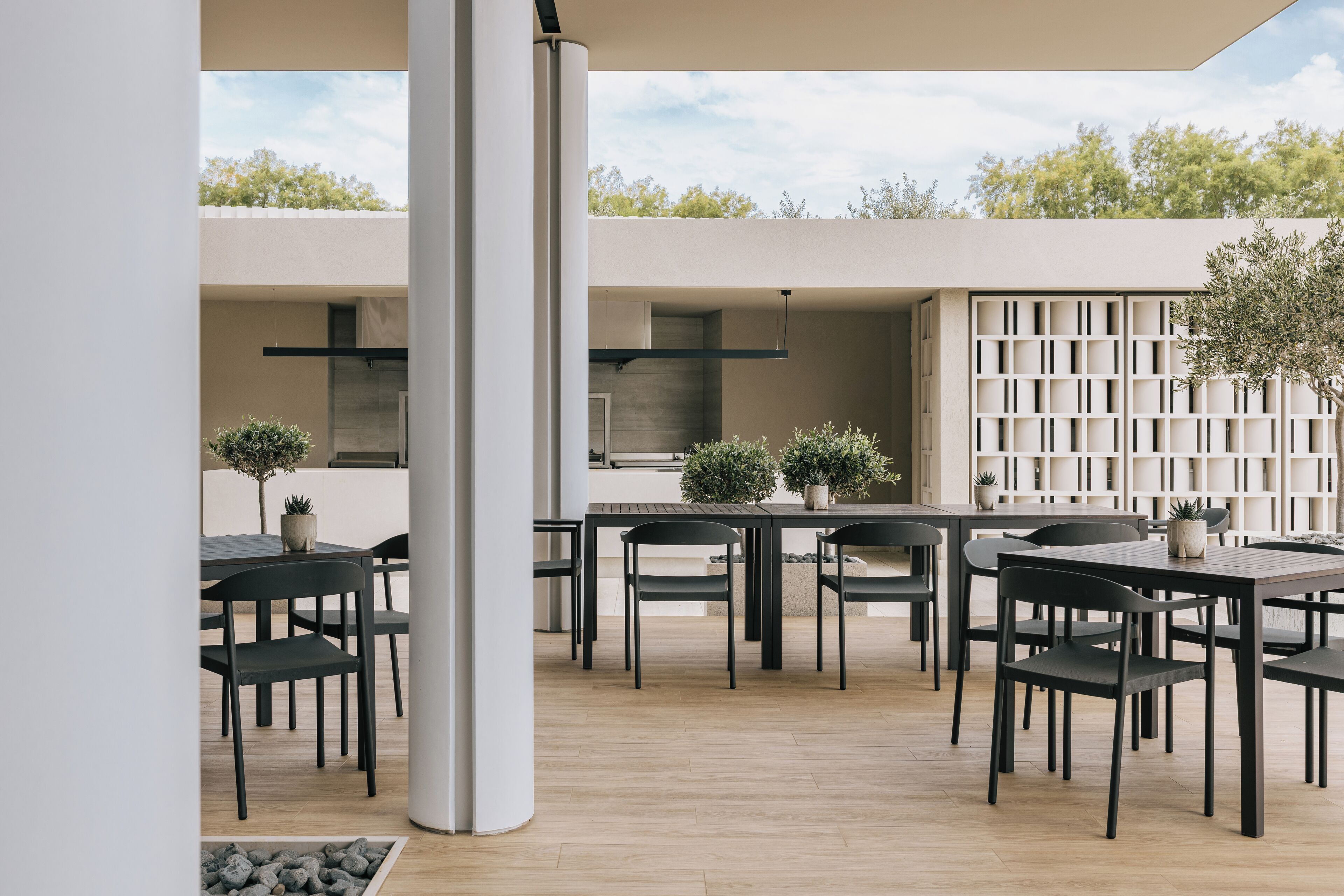 An outdoor dining area with multiple tables and chairs, a wooden floor, and a view of the sky and trees.
