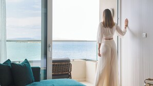 A room with a large glass door leading to a balcony with a view of the sea. - Divani Apollon Palace & Thalasso (Vari-Voula-Vouliagmeni)