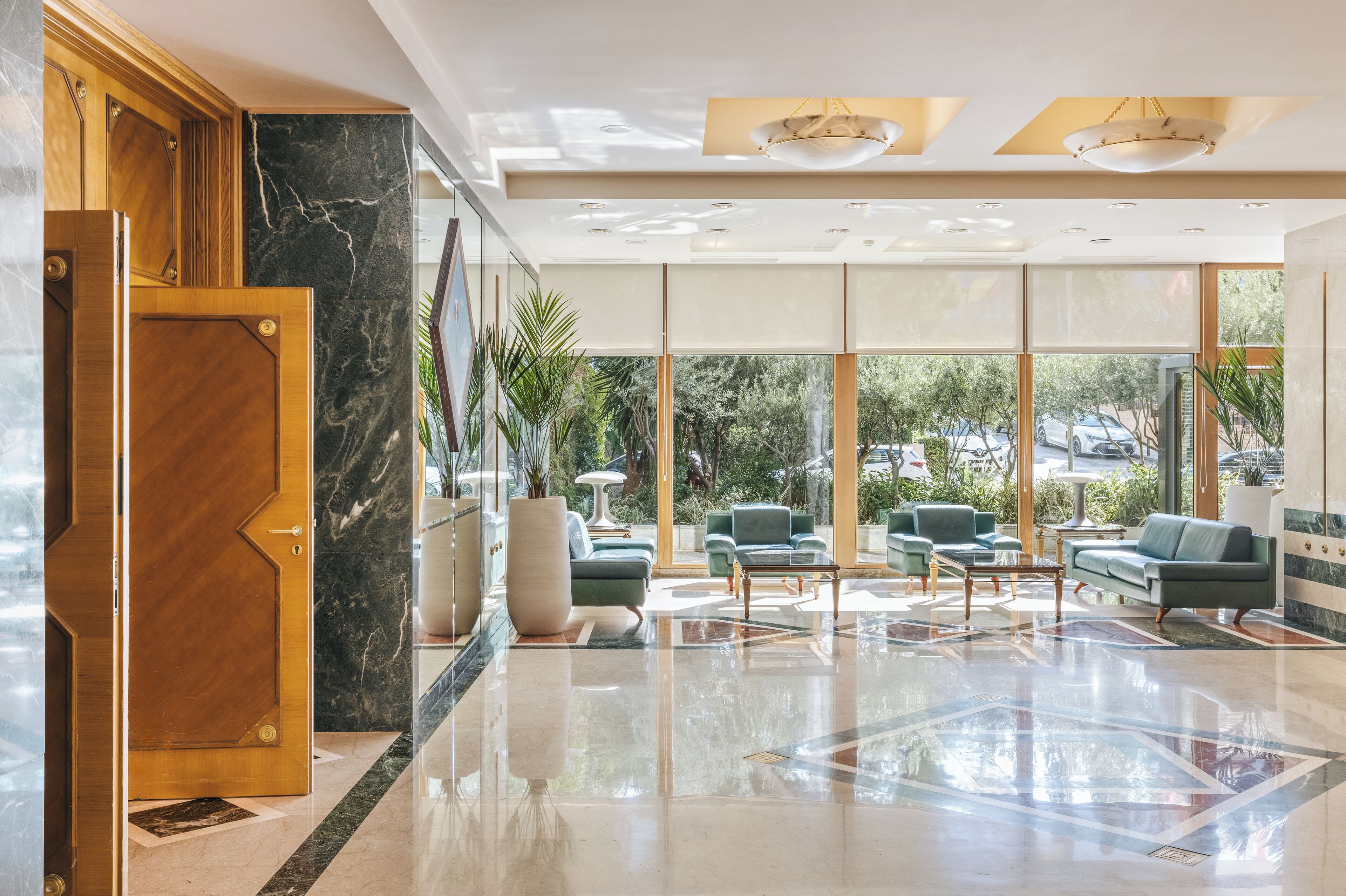A spacious lobby with a marble floor, green seating area, and large windows offering a view of the outdoors.