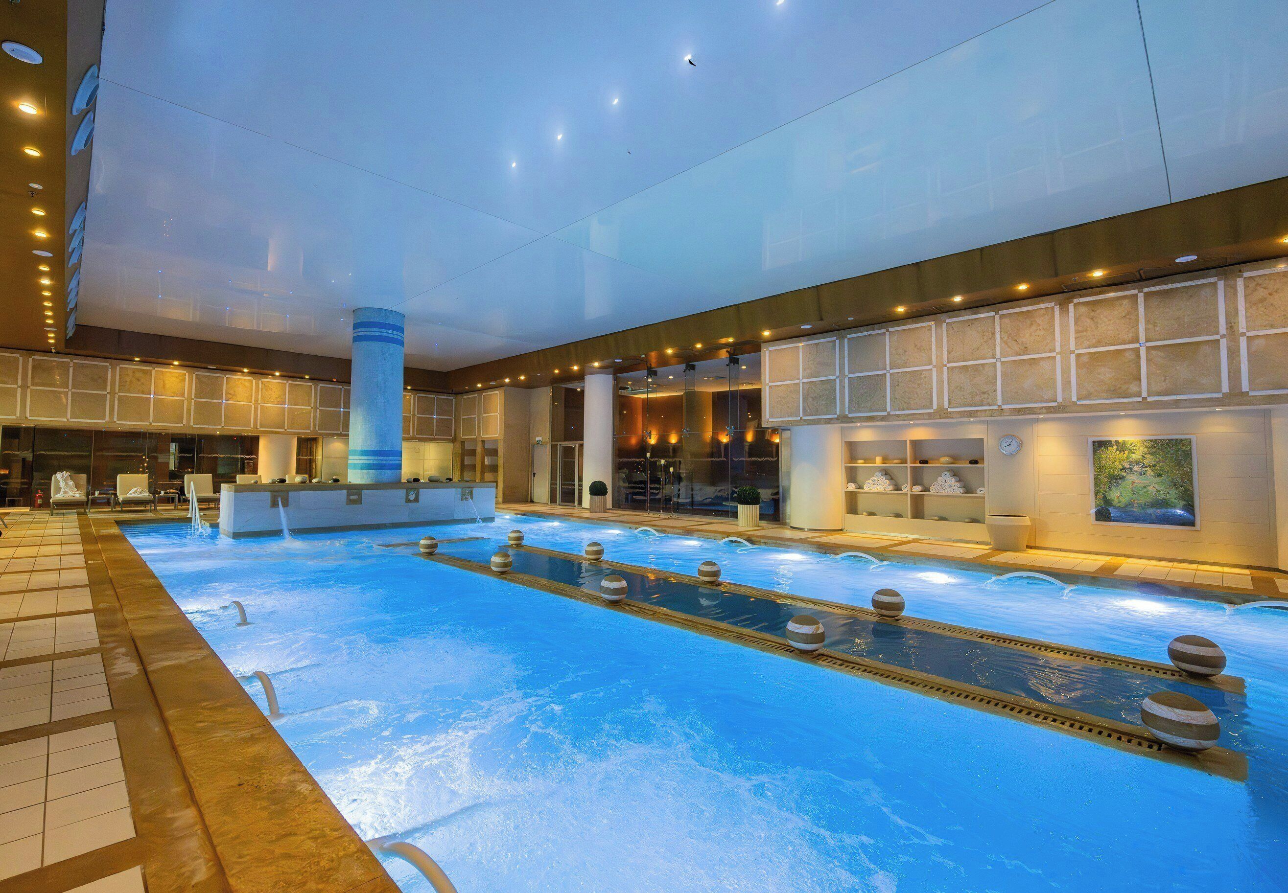 Ein Hallenbad mit einer zentralen Wasserspüle, umgeben von Liegestühlen und einer Rezeption.
