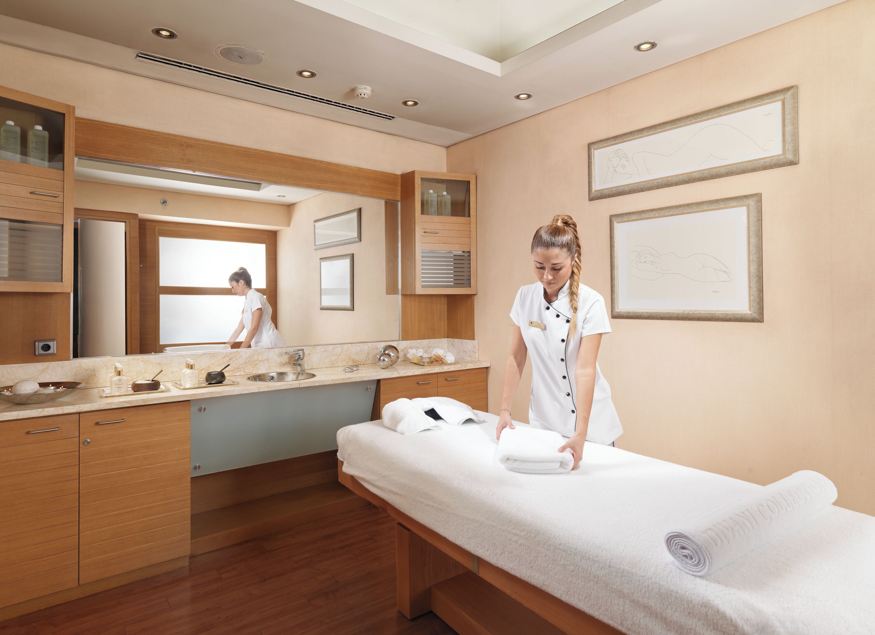 A modern hotel room with a wooden vanity, a large mirror, a massage table, and a well-lit bathroom.