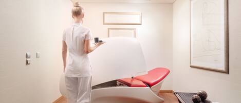 A modern spa room with a massage table, a framed artwork on the wall, and a tray with a cup and a small object.