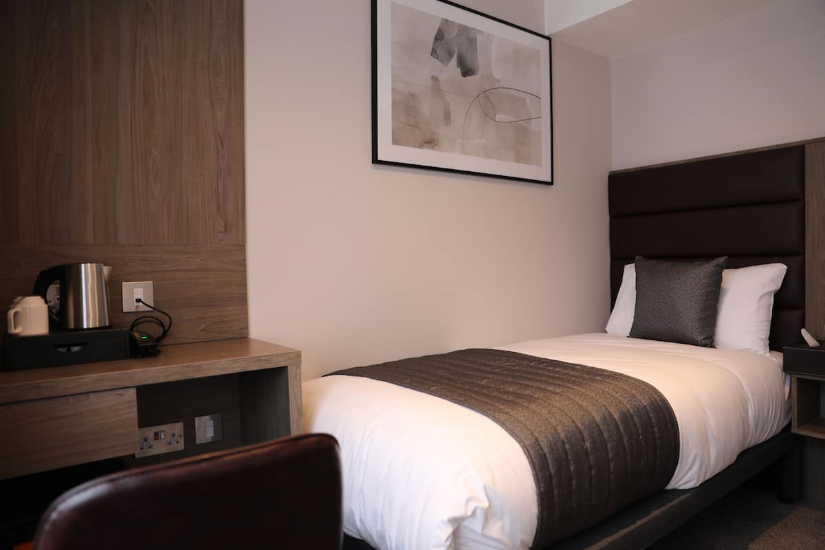 Ein Hotelzimmer mit einem Bett, einem Schreibtisch mit Kaffeemaschine und einem gerahmten abstrakten Kunstwerk an der Wand.